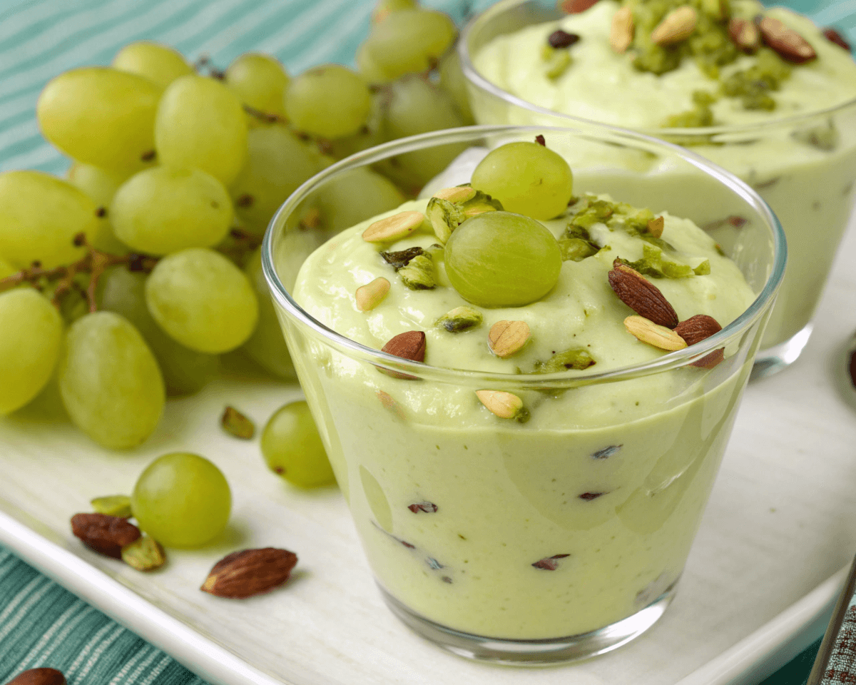 Creamy pistachio pudding with grapes and nuts in glass cups.